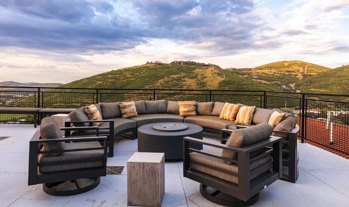 An outdoor terrace with cushioned seating and rolling green hills beyond the railing.
