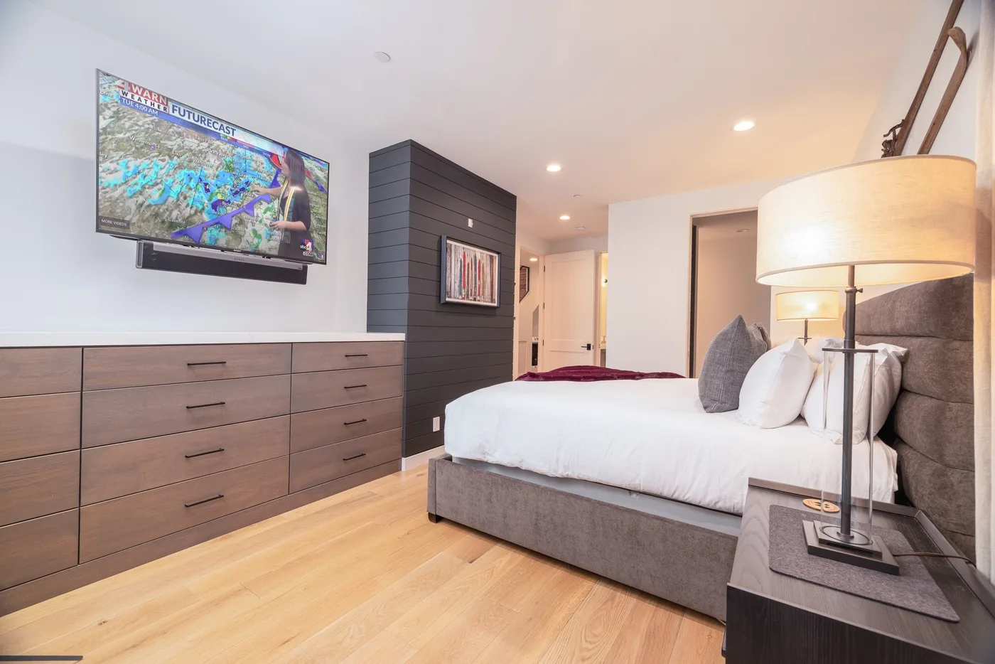 A bedroom with a bed, wood flooring, and a wall-mounted television.