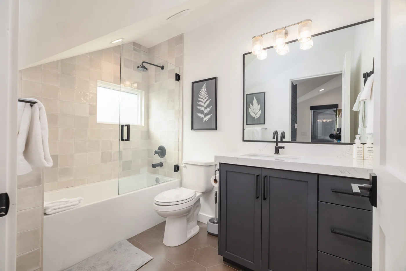 A bathroom with a glass shower screen, bathtub, toilet, and dark vanity.