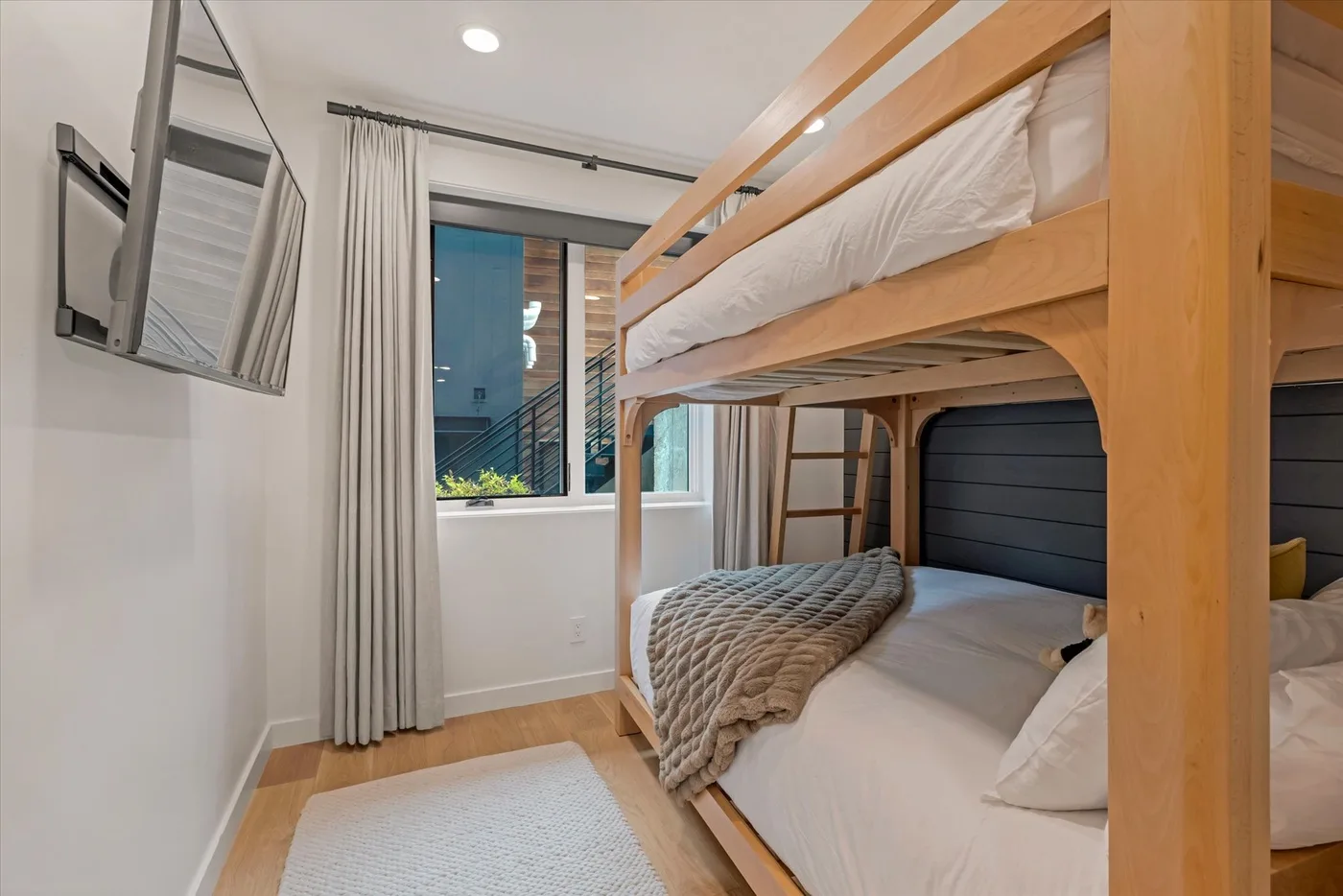 A bedroom with a wooden bunk bed beside a window.