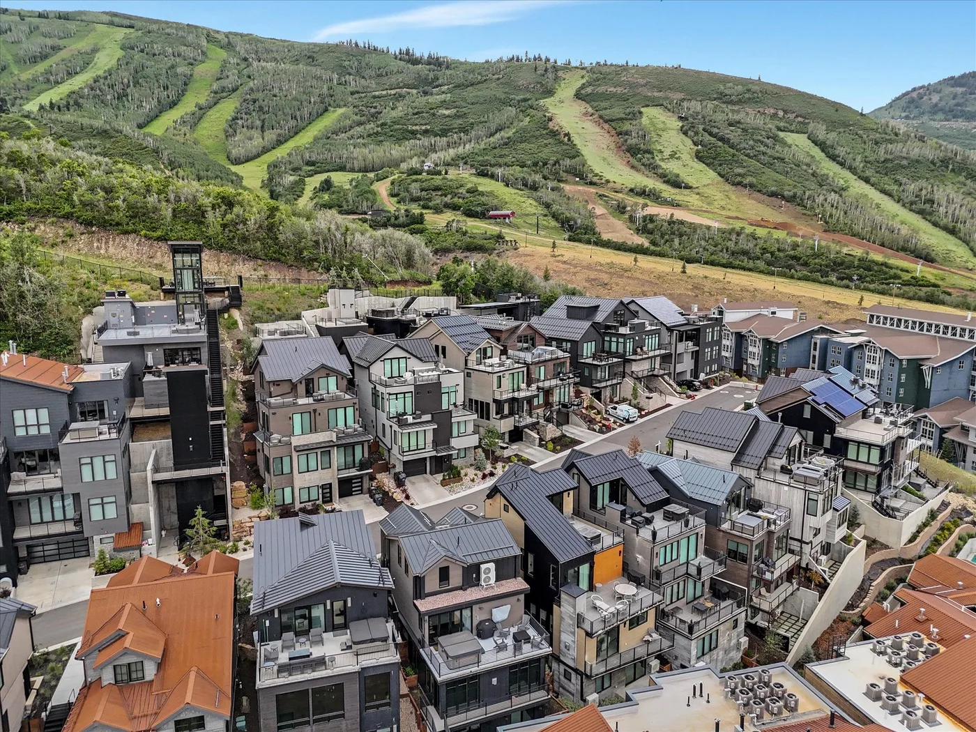 A hillside neighborhood of modern buildings sits below green ski trails.