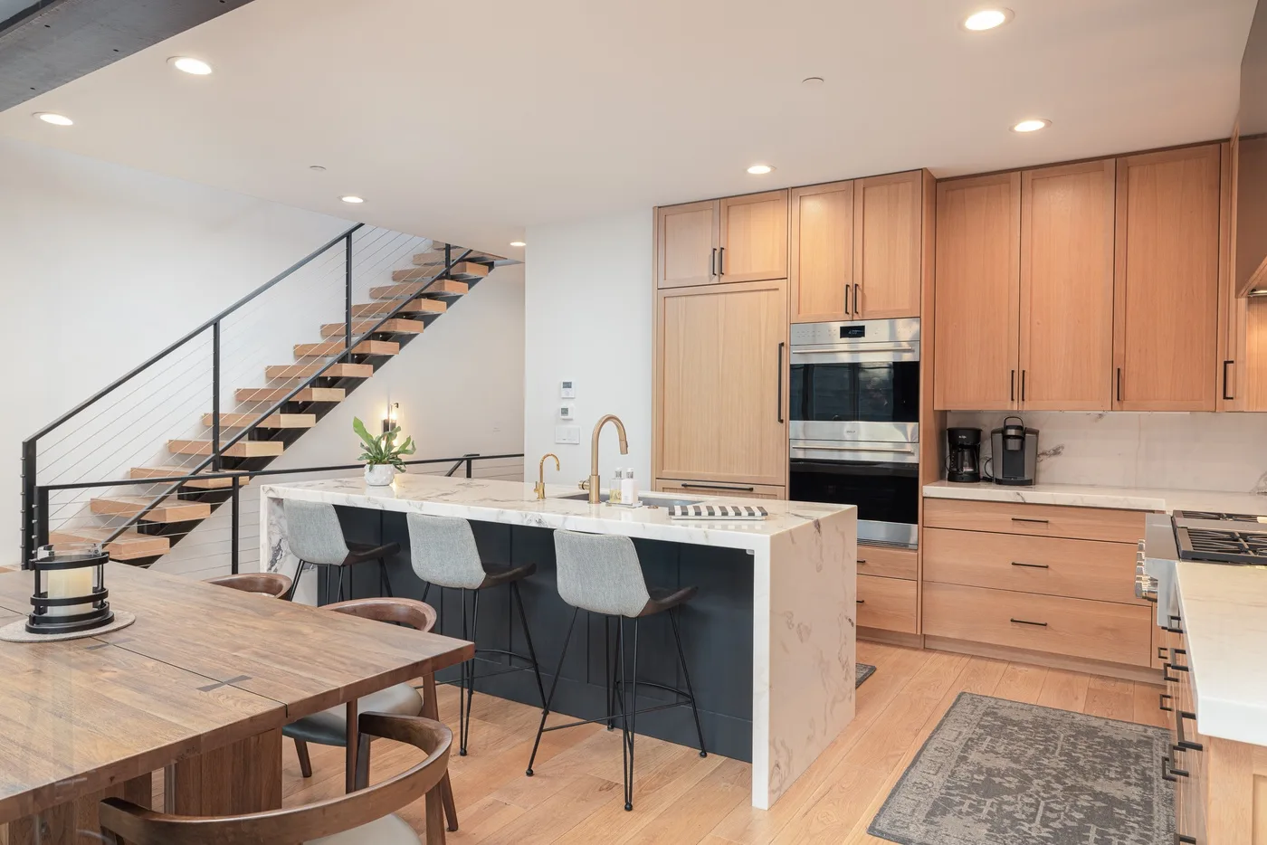 A modern kitchen with a large island, bar seating, and an open staircase.