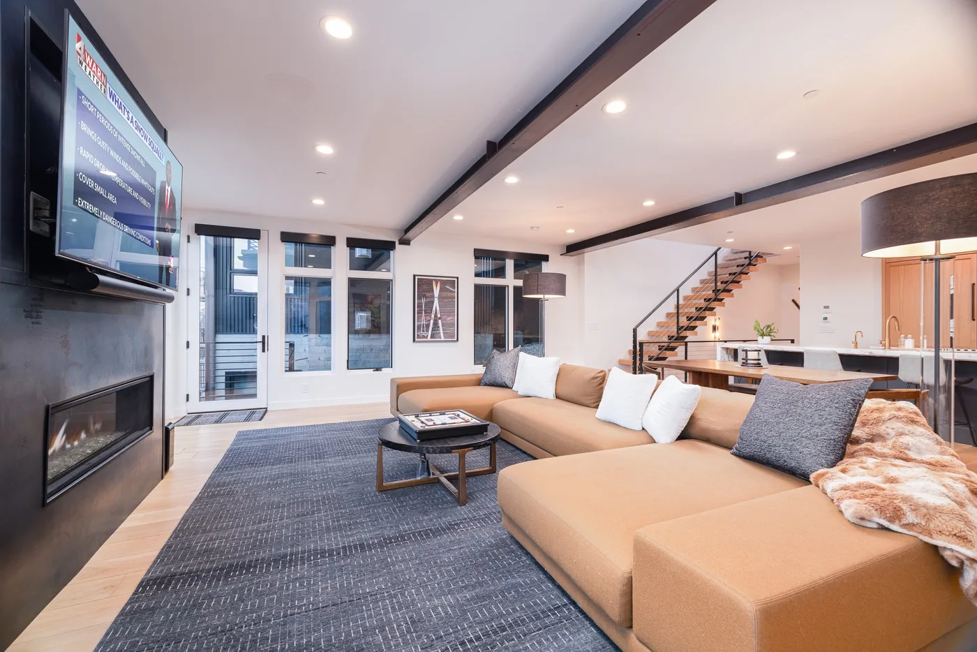 A modern living room with sectional seating, a television, and an open staircase.