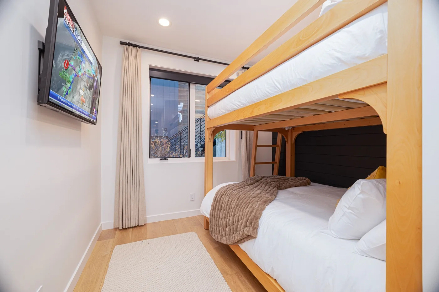 A bedroom with a wooden bunk bed, white bedding, and a window.