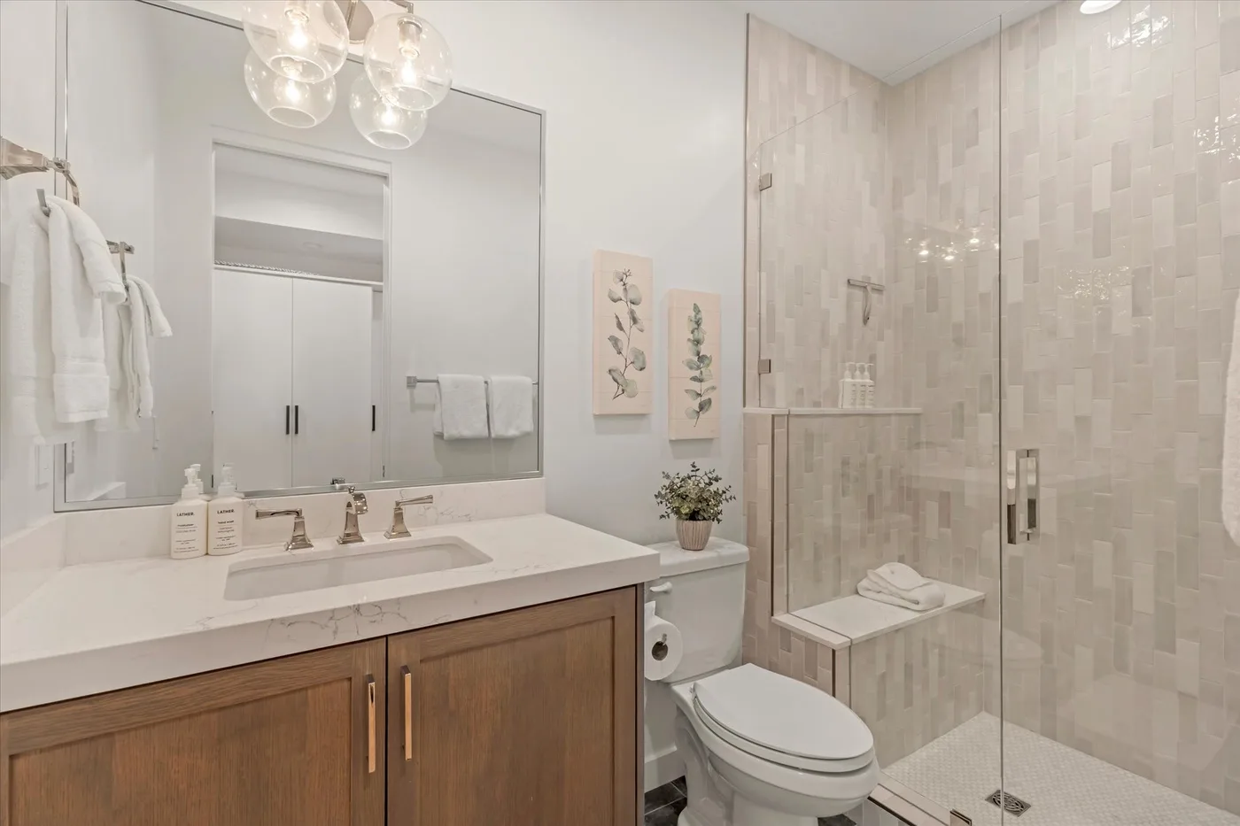 A bright bathroom with a vanity, toilet, and glass-enclosed shower.
