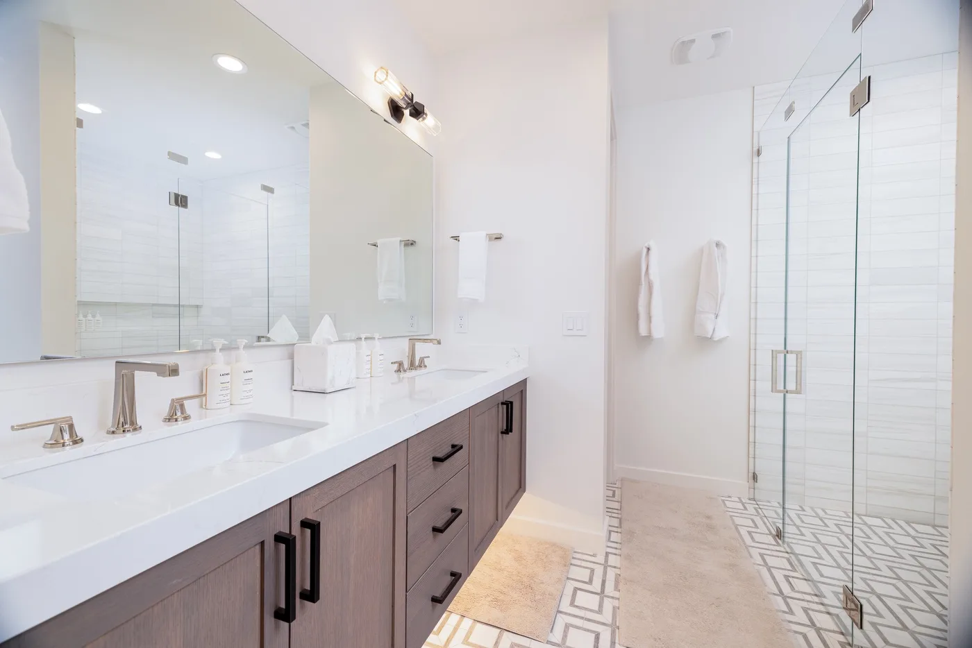 A bright bathroom with a long vanity, wide mirror, and glass shower.