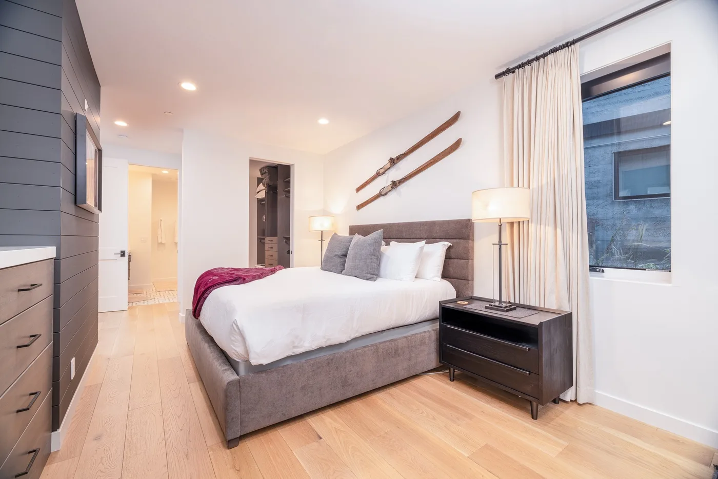 A bright bedroom with a neatly made bed, bedside tables, and curtains by the window.