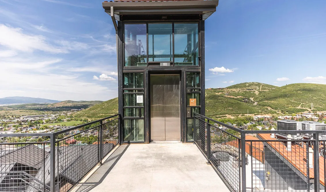 An outdoor elevator entrance stands at the end of a raised walkway overlooking hills.