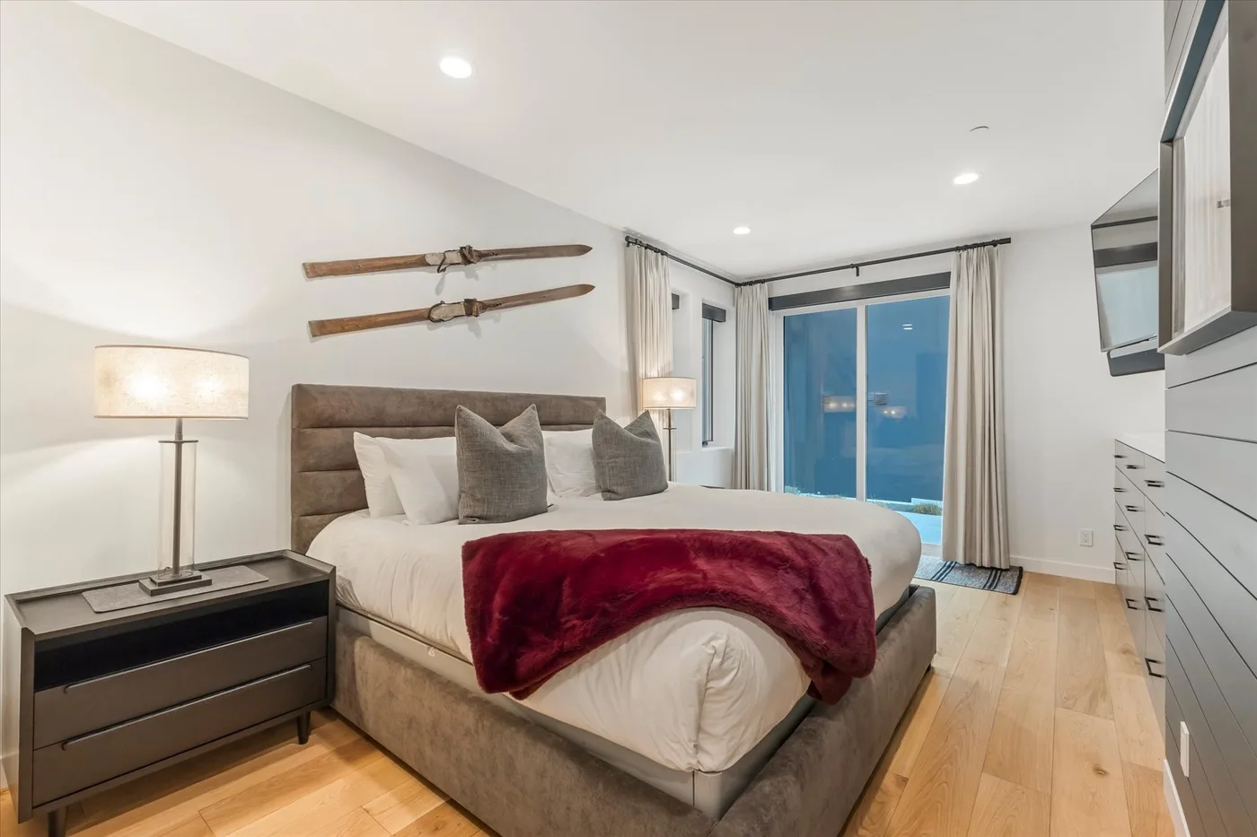 A bedroom with a large bed, bedside table, and glass doors.