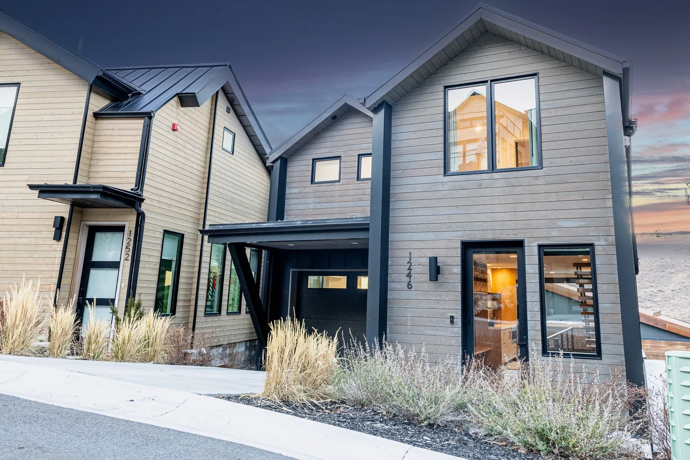 Modern multi-story house exterior with gray siding and large windows at dusk.
