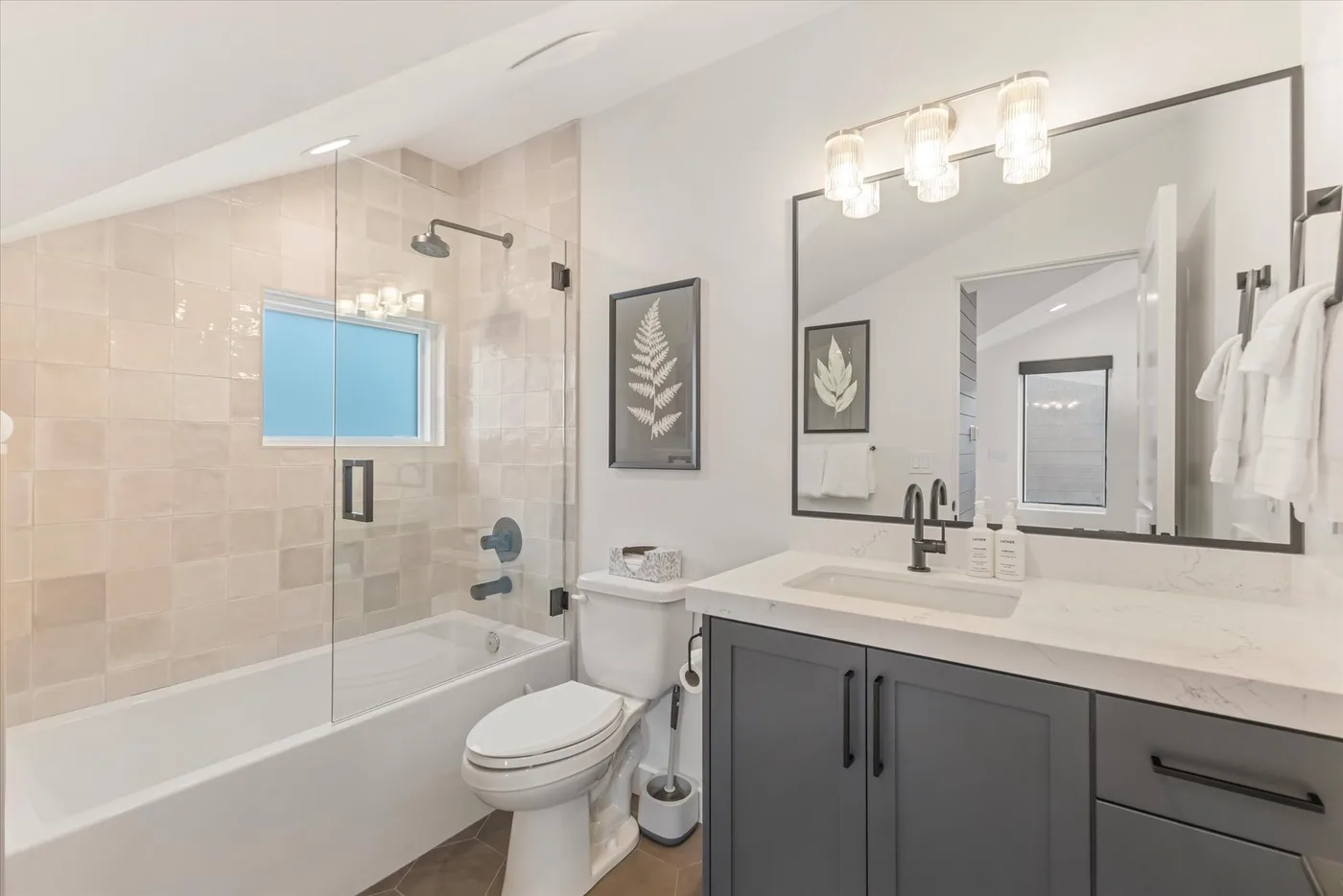 A bathroom with a bathtub, toilet, and vanity beneath a large mirror.
