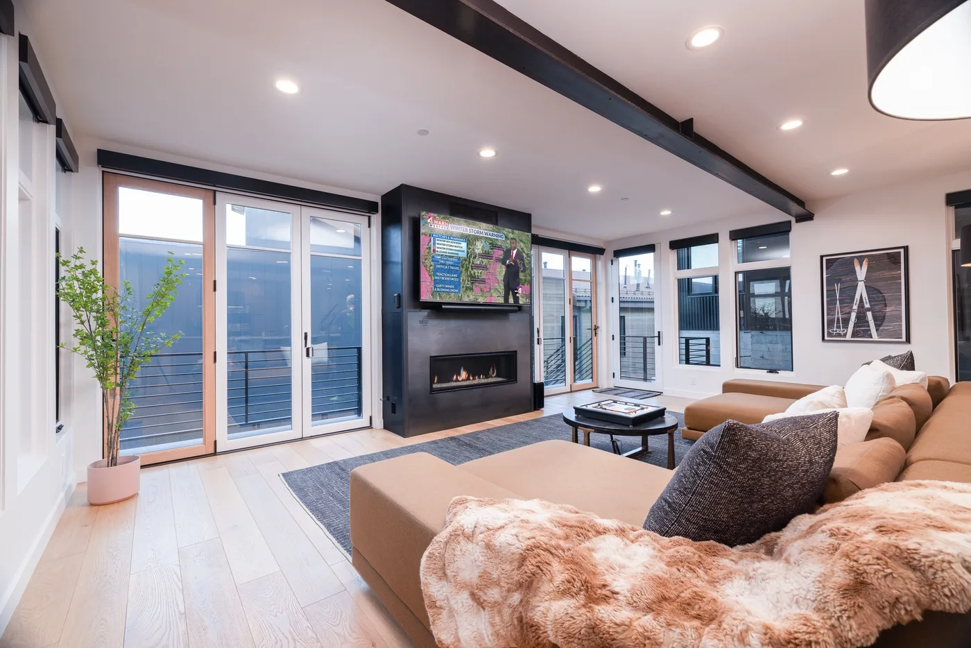 A bright living room with seating, large windows, and a wall-mounted television.