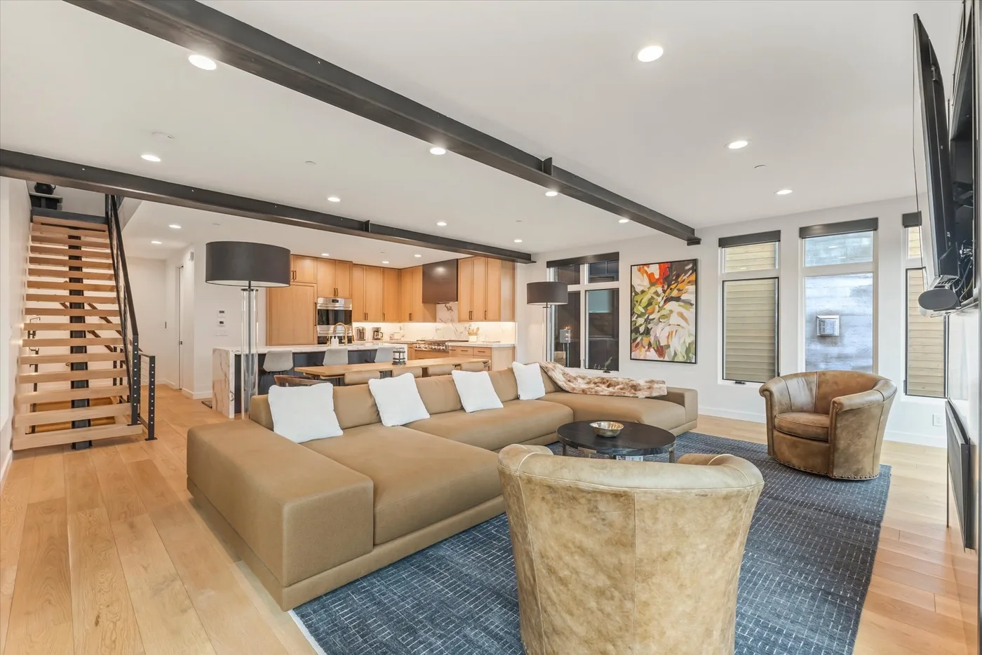 An open-plan living room with seating, a coffee table, and a kitchen in the background.