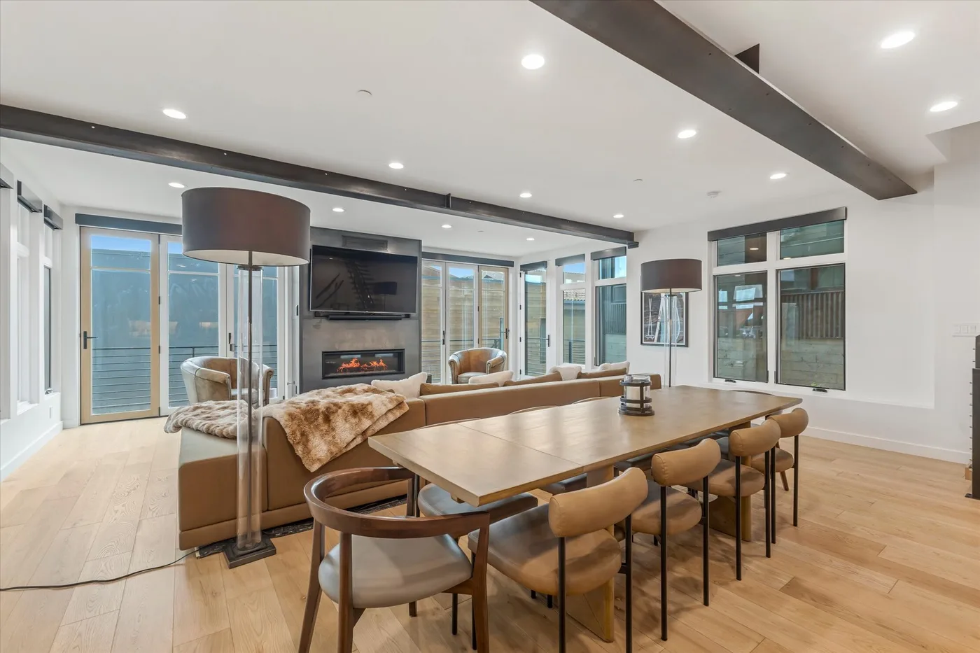A bright open-plan living and dining room with a long table and fireplace.