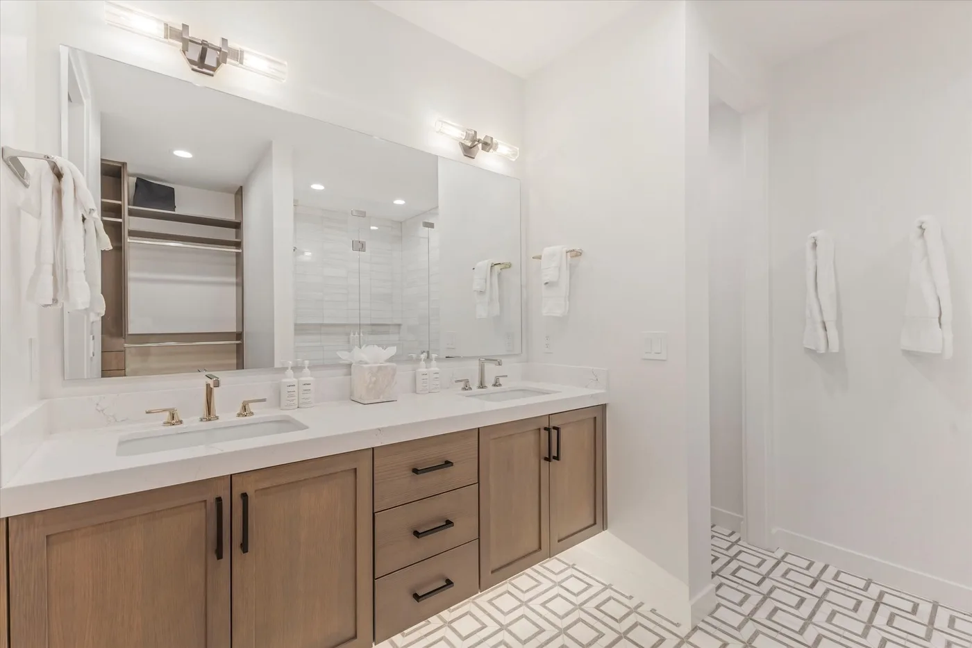 A bright bathroom features a long vanity, large mirror, and walk-in shower.