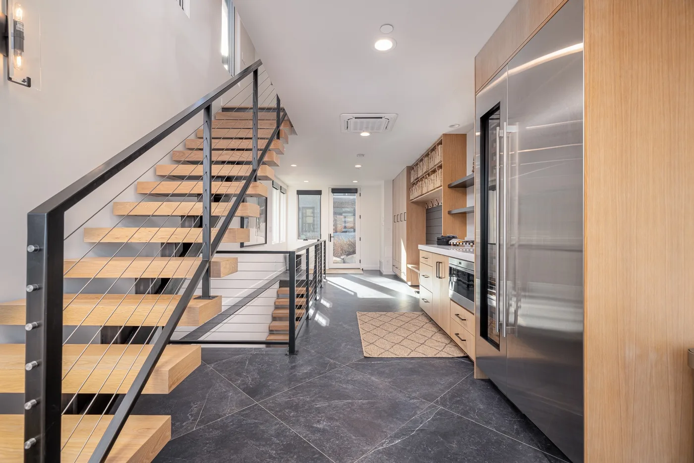 A modern kitchen and dining area with an open staircase and dark tiled floor.