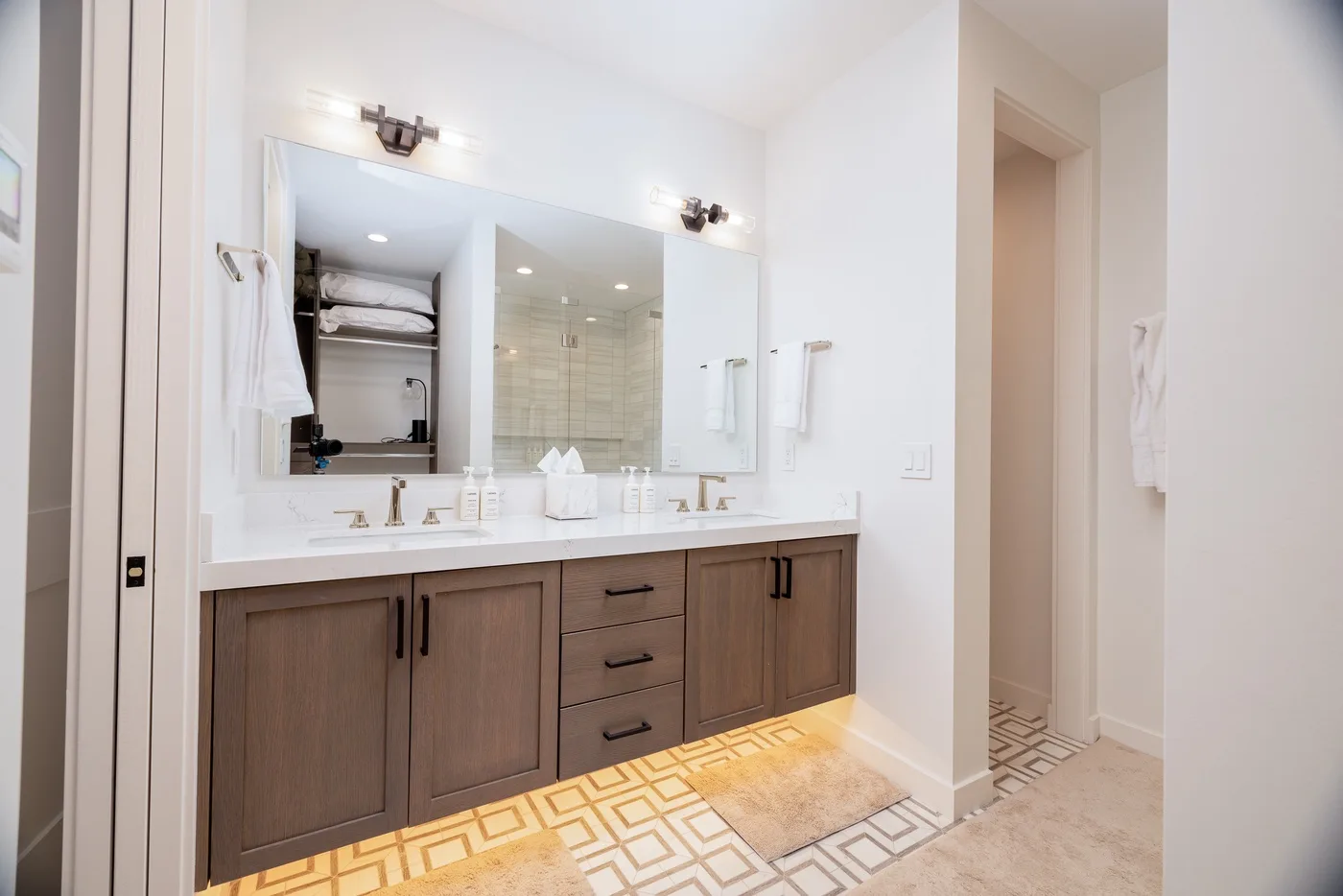 A bright bathroom vanity with a wide mirror and patterned tile flooring.
