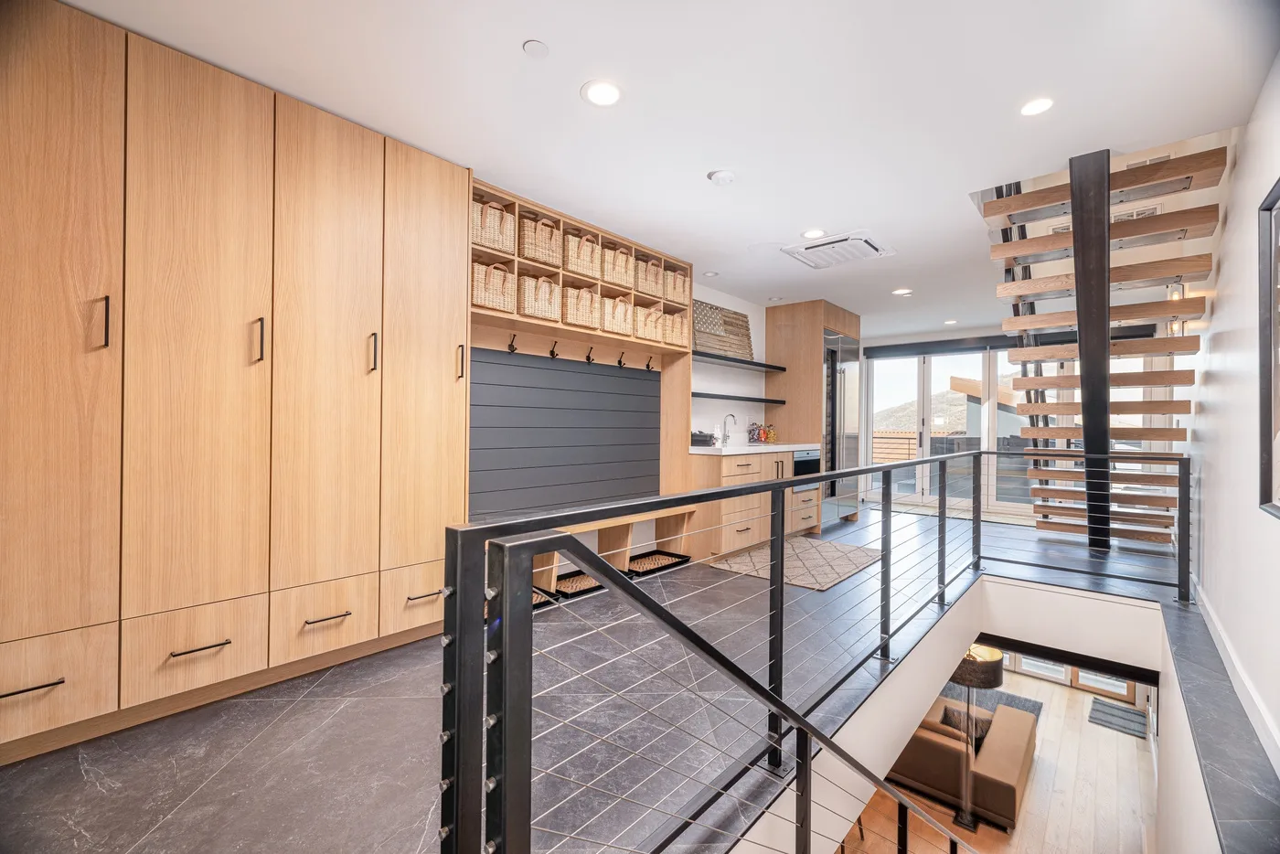 A modern interior hallway with wood cabinetry and a metal railing overlooking the lower level.