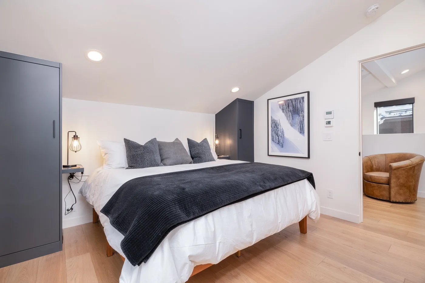 A bedroom with a large bed, dark bedding, and framed wall art.