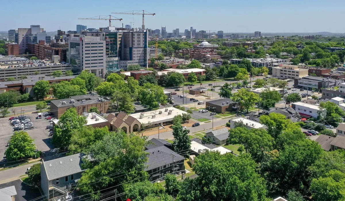 Vista aérea de un barrio urbano arbolado con edificios de oficinas a lo lejos.