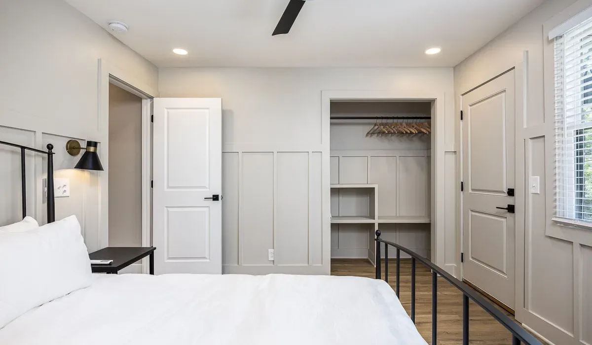 Un dormitorio luminoso con una cama blanca y un armario abierto.