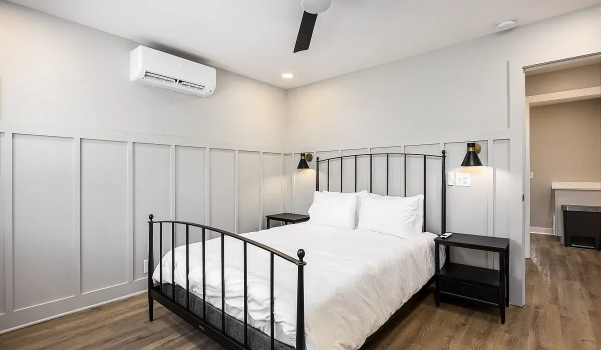 Un dormitorio luminoso con cama blanca, estructura metálica negra y suelo de madera.