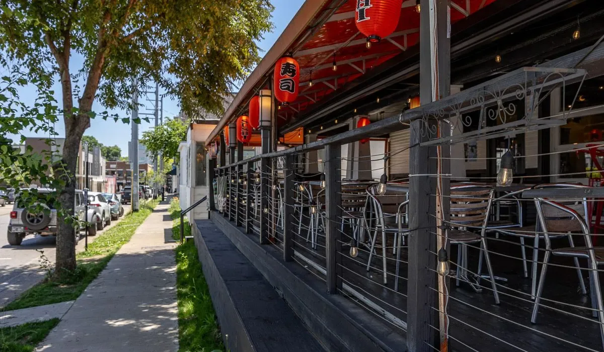 Una terraza exterior de restaurante con asientos metálicos y faroles rojos.