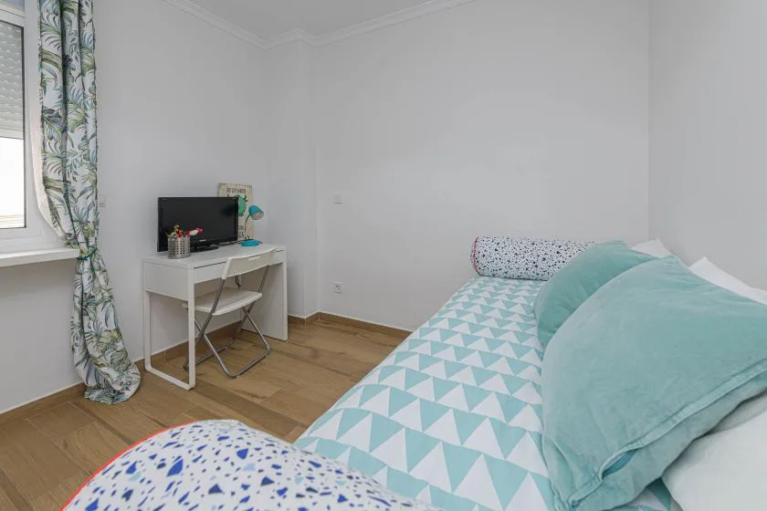 Un dormitorio con una cama cubierta con ropa de cama geométrica turquesa y blanca.