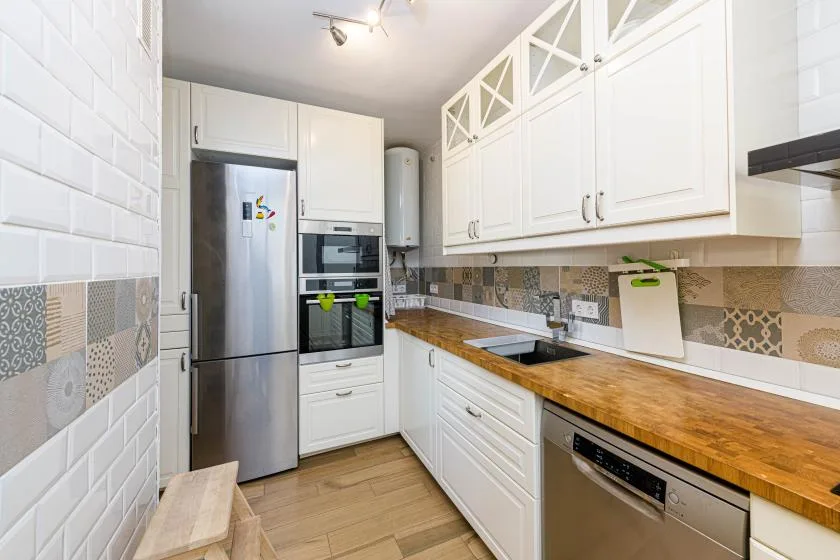 Una cocina luminosa con gabinetes blancos, electrodomésticos de acero inoxidable y una encimera de madera.