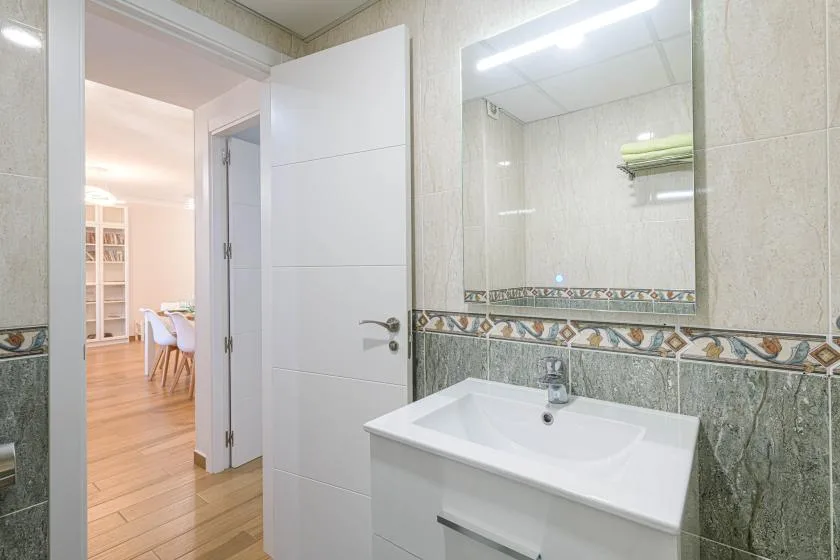 Un baño luminoso con un lavabo blanco y una puerta abierta hacia un comedor.