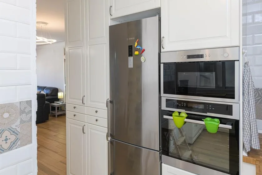 Una cocina blanca con un refrigerador de acero inoxidable y hornos empotrados.