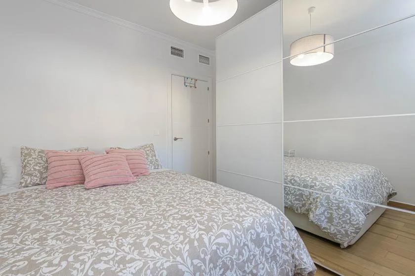 Un dormitorio con ropa de cama estampada, almohadas rosas y puertas de armario espejadas.