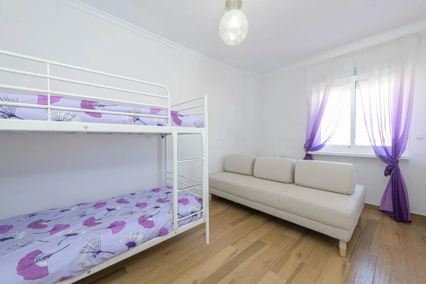 Un dormitorio luminoso con literas y un sofá junto a una ventana con cortinas.