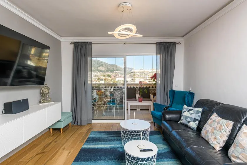 Sala de estar con asientos, un televisor y puertas corredizas de vidrio que dan a un balcón.