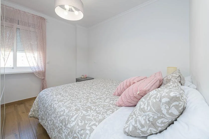 Un dormitorio con una cama vestida con ropa de cama estampada gris y almohadas rosas.