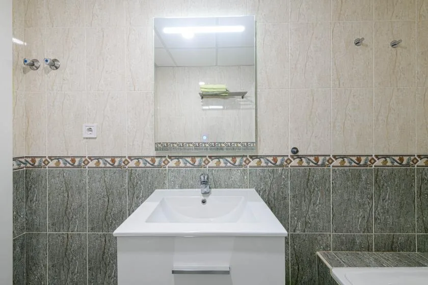 Un lavabo de baño con espejo frente a paredes alicatadas.