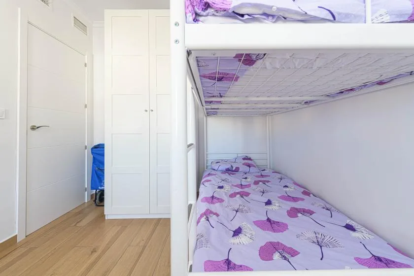 Una zona de descanso con literas y ropa de cama estampada en tonos morados, junto a un armario blanco.