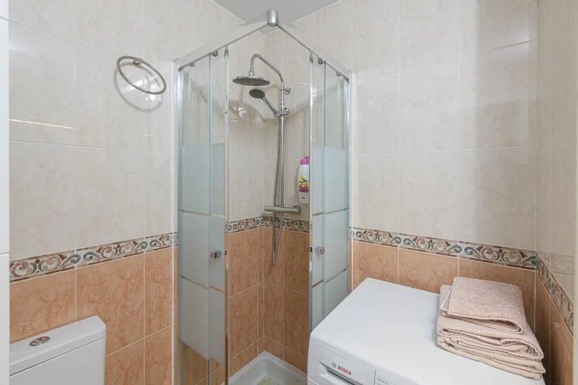 Un baño alicatado con una ducha de vidrio y una lavadora.