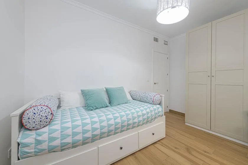 Un dormitorio con una cama de día cubierta con ropa de cama geométrica y espacio de almacenamiento integrado.