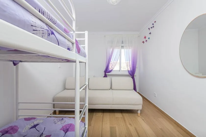 Un dormitorio luminoso con una litera, un sofá y cortinas moradas.