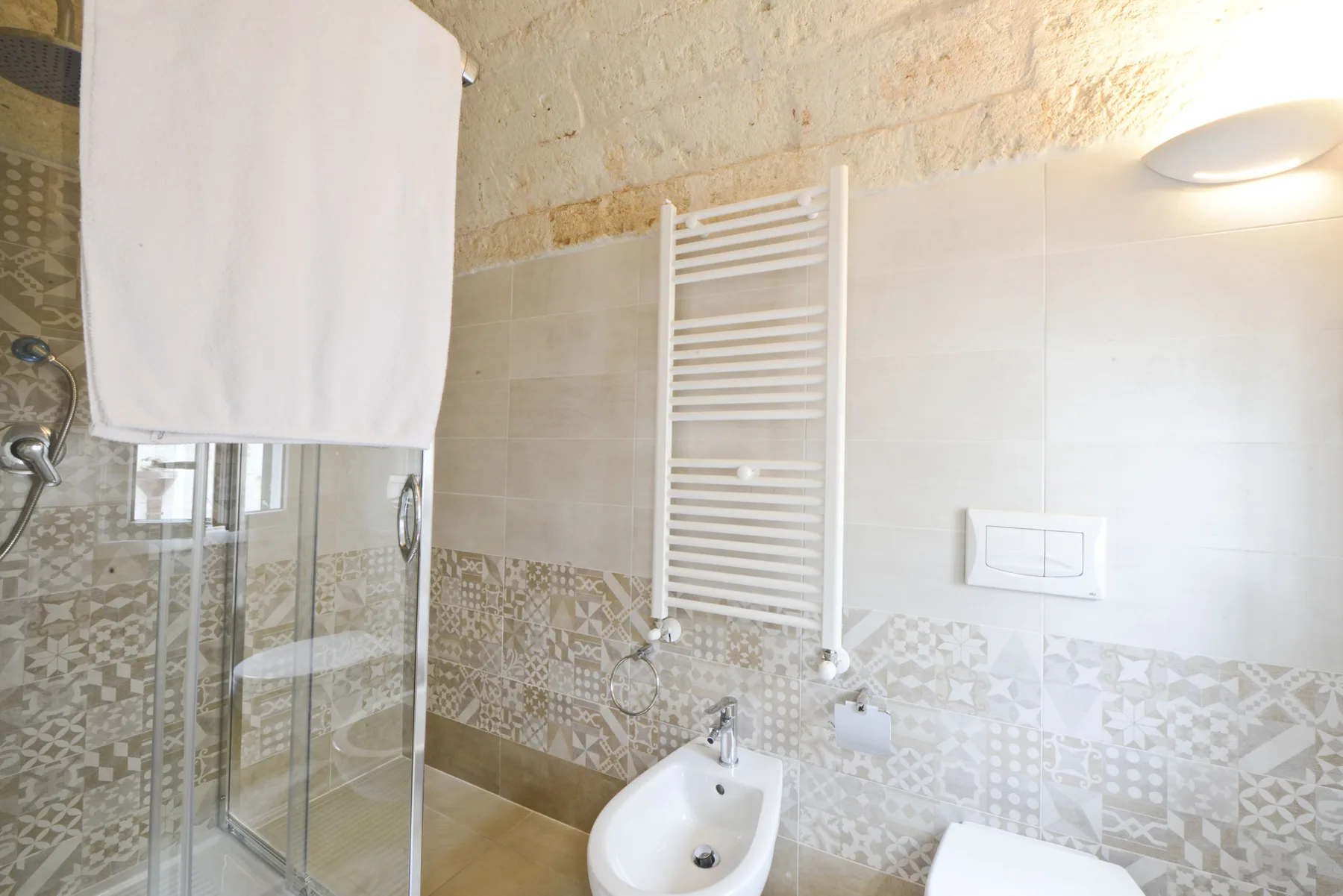 Un baño con azulejos, ducha de vidrio y toallero calefactable en la pared.