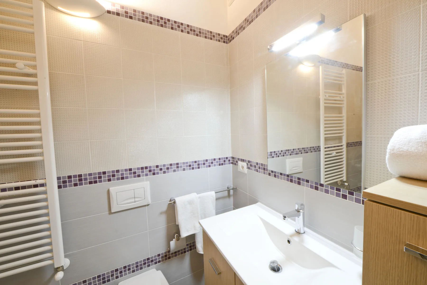 Un baño alicatado con lavabo, espejo y toallero calefactor.