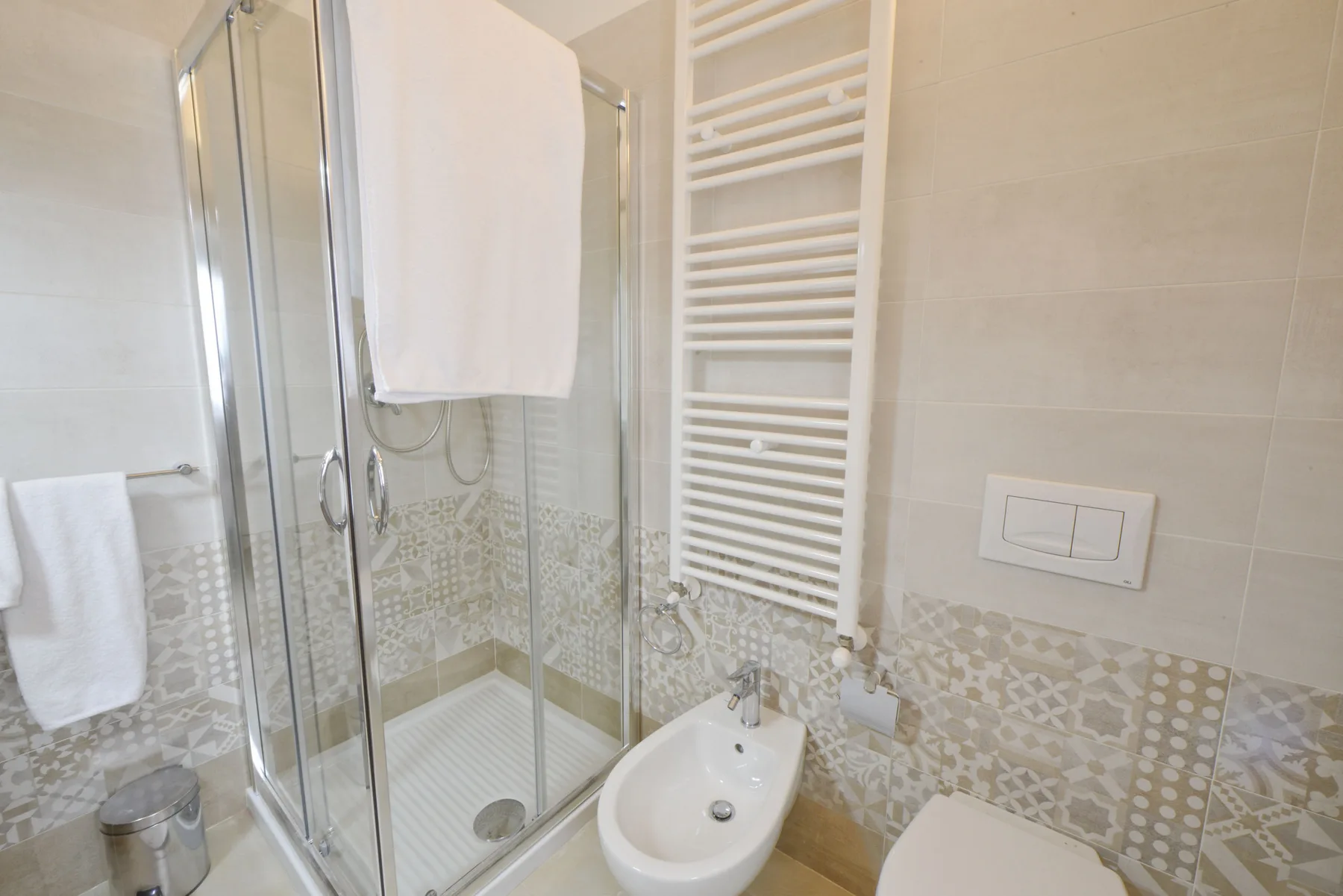 Un baño revestido de azulejos con ducha de vidrio y toallero calefactable en la pared.