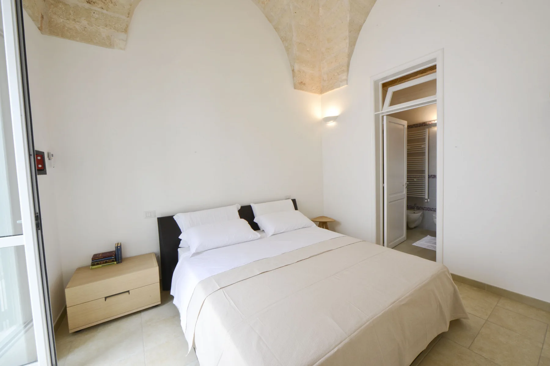 Un dormitorio luminoso con una cama bien tendida y una puerta al baño.