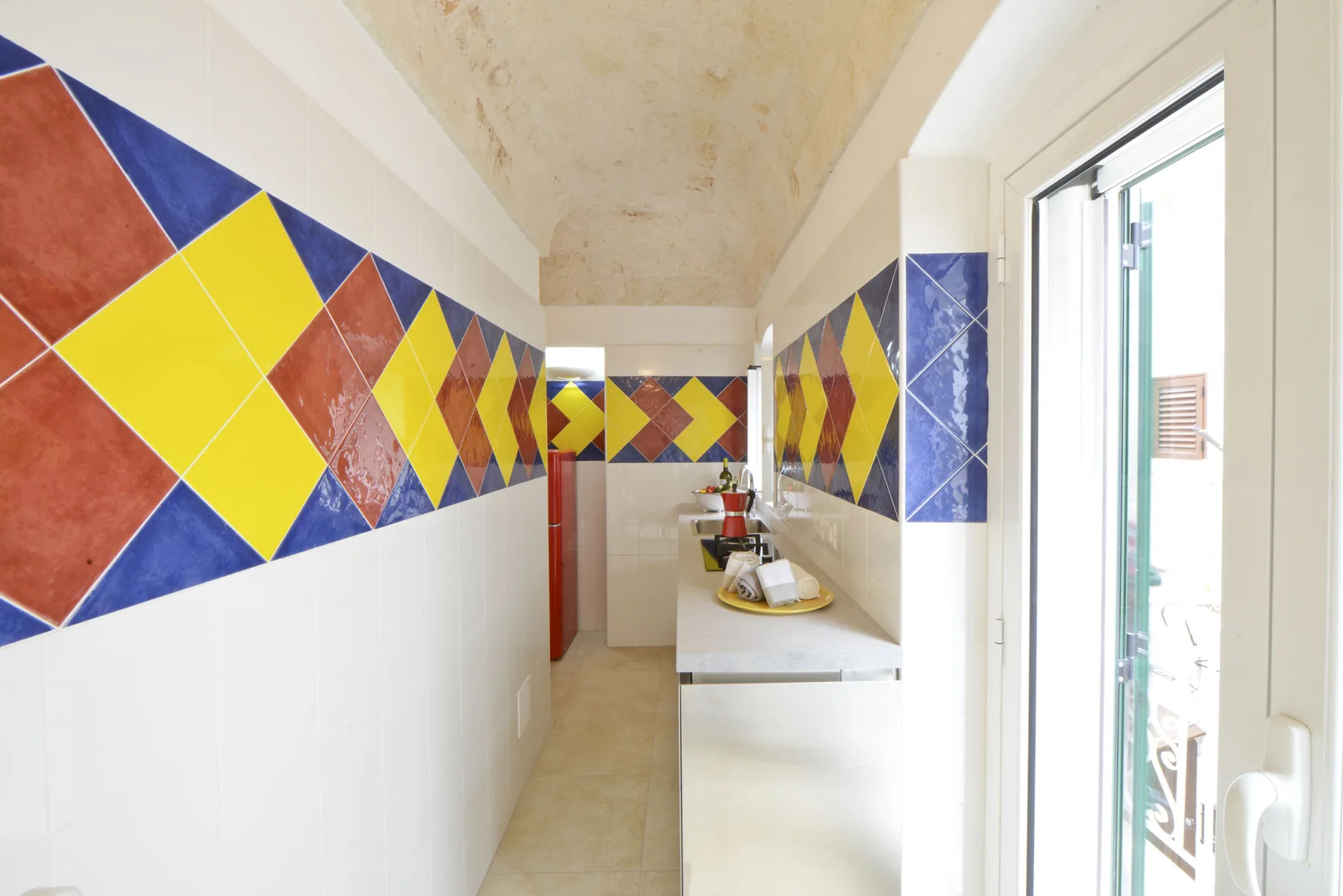 Un baño estrecho con una encimera larga y paredes de azulejos geométricos de colores.
