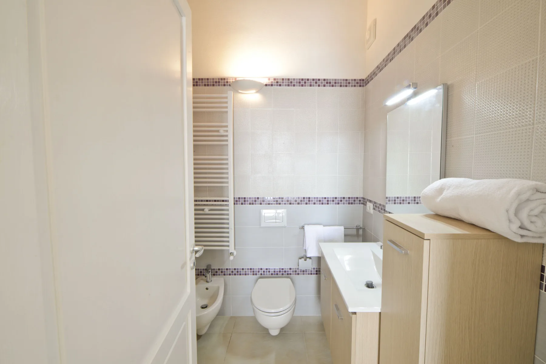 Un baño con azulejos, inodoro, lavabo y radiador para toallas.