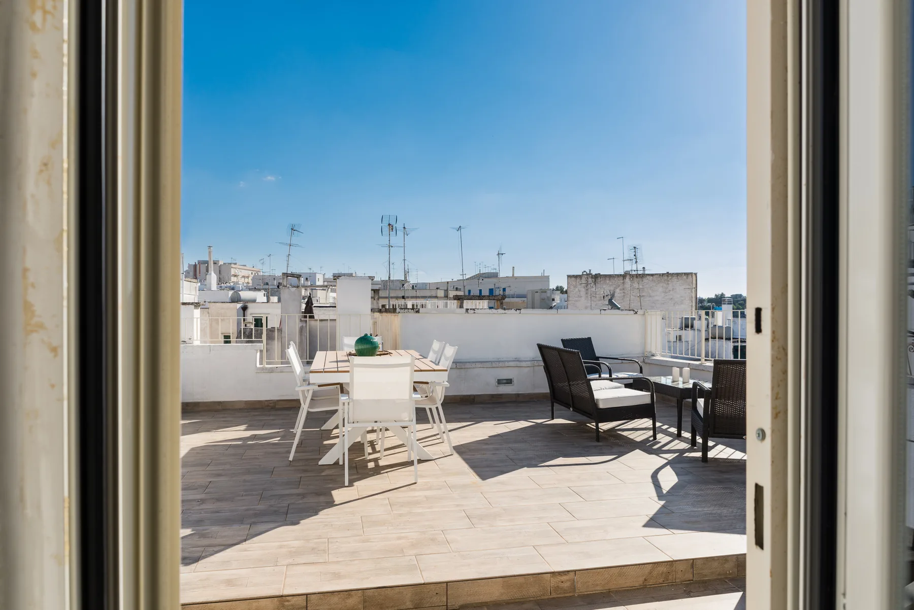 Una terraza en la azotea con asientos y una mesa al aire libre da a edificios cercanos.