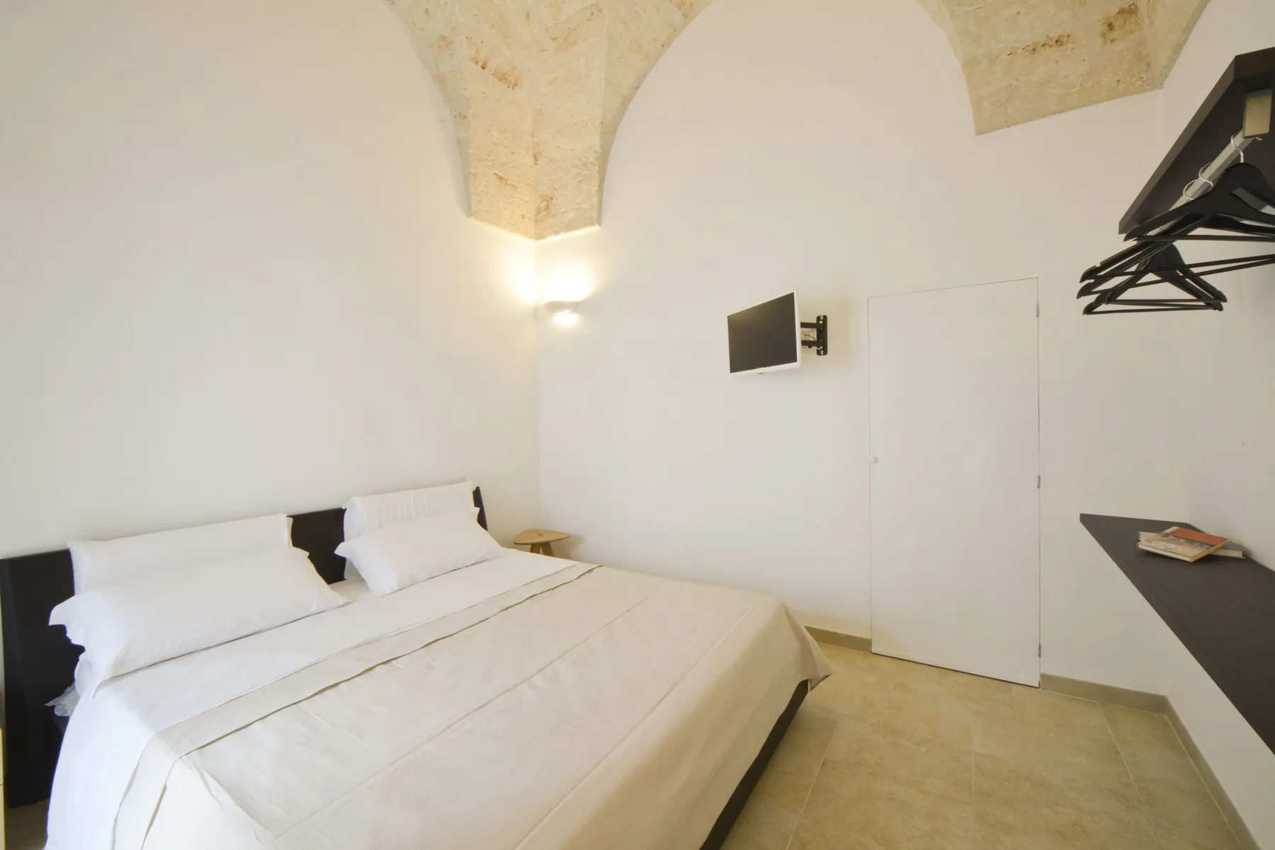 A bedroom with a neatly made bed, white walls, and an arched ceiling.