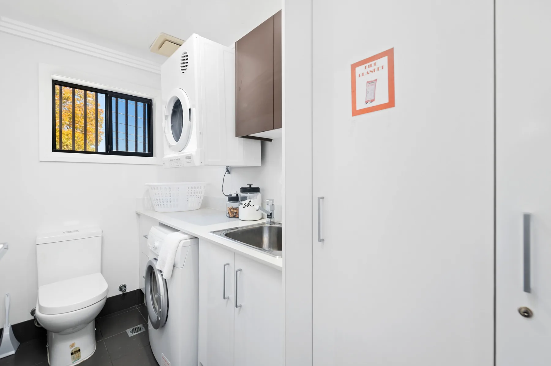 Un baño con inodoro, lavabo y electrodomésticos de lavandería apilados.