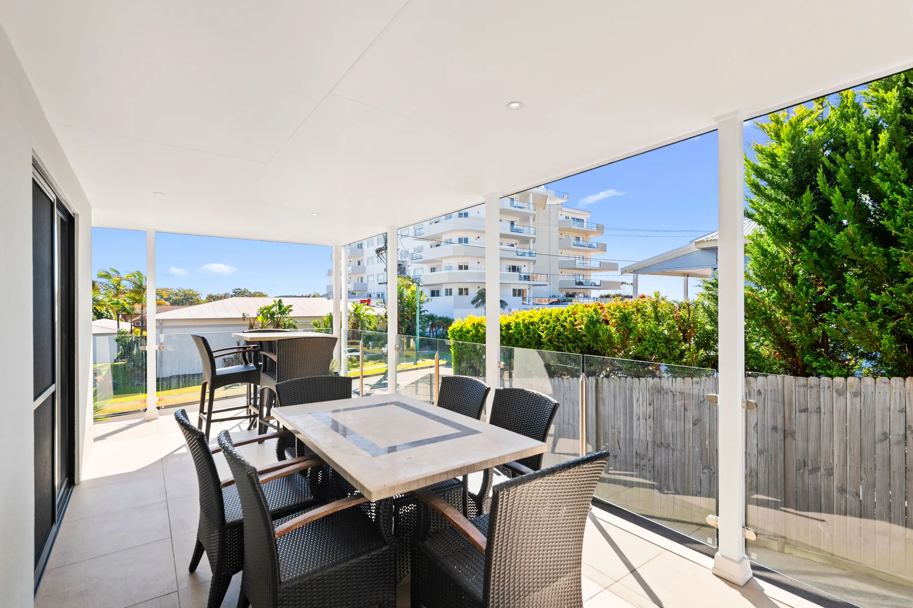 Comedor exterior cubierto con una mesa y asientos junto a paneles de vidrio.